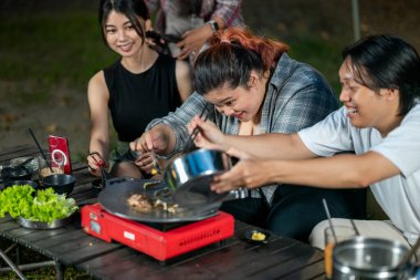 Endonezyalı güneydoğu Asyalılar ellerinde maşayla soğanlı ızgara tavada marine edilmiş et bulgogi pişiriyorlar. Doğal ortamdaki yemekten zevk alma sahnesi.