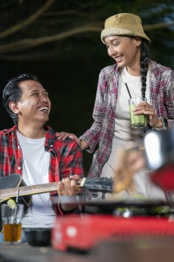 Endonezyalı güneydoğu Asyalı bir adam arkadaşlarıyla dışarıda akustik gitar çalıyor. Rahat ve keyifli bir yaşam tarzı gösteriyorum. Kamp yapmanın doğal ortamında keyif alma sahnesi.