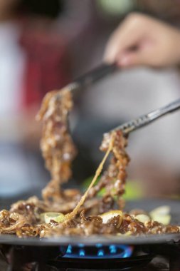 Dilimlenmiş et bulgogi pişirip soğanlı ızgara tavada pişiren insanların yakın görüntüsü. Doğal ortamdaki yemekten zevk alma sahnesi.