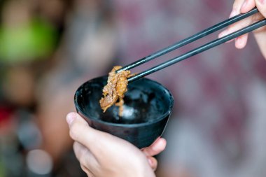 Yemeklerden zevk alan insanlar, yemek çubuklarını kullanarak kendilerine küçük siyah kaselerden ızgara yemek servisi yaparlar. Doğal ortamdaki yemekten zevk alma sahnesi.