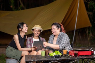 Endonezyalı güneydoğu Asyalı kadınlar gece kamp yaparken tablet ekrana bakarlar. Doğal ortamdaki kamp hayatı sahnesi.