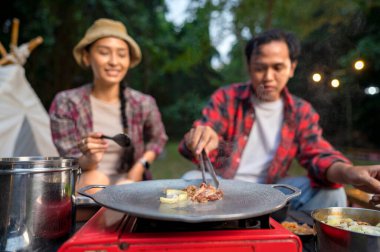 Endonezyalı güneydoğu Asyalı çift ellerinde maşayla soğanlı ızgara tavada marine edilmiş et bulgogi pişiriyorlar. Doğal ortamdaki yemekten zevk alma sahnesi.
