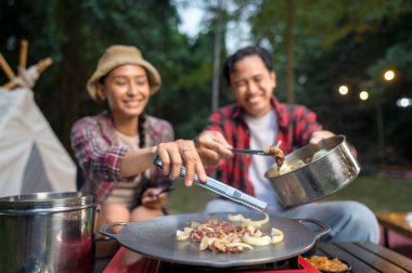 Endonezyalı güneydoğu Asyalı çift ellerinde maşayla soğanlı ızgara tavada marine edilmiş et bulgogi pişiriyorlar. Doğal ortamdaki yemekten zevk alma sahnesi.