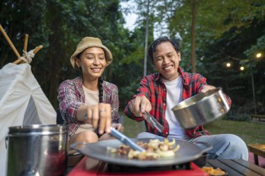 Endonezyalı güneydoğu Asyalı çift ellerinde maşayla soğanlı ızgara tavada marine edilmiş et bulgogi pişiriyorlar. Doğal ortamdaki yemekten zevk alma sahnesi.