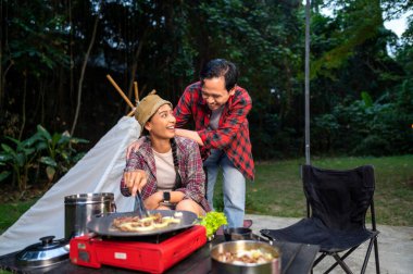 Endonezyalı güneydoğu Asyalı çift ellerinde maşayla soğanlı ızgara tavada marine edilmiş et bulgogi pişiriyorlar. Doğal ortamdaki yemekten zevk alma sahnesi.
