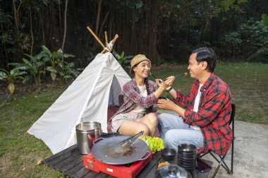 Endonezyalı güneydoğu Asyalı çift yemek çubuklarıyla yemek paylaşıyor. Kamp yaparken gülümseyip birlikte olmanın tadını çıkarıyor. Doğal ortamdaki yemekten zevk alma sahnesi.