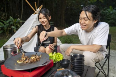 Endonezyalı güneydoğu Asyalı çift ellerinde maşayla soğanlı ızgara tavada marine edilmiş et bulgogi pişiriyorlar. Doğal ortamdaki yemekten zevk alma sahnesi.
