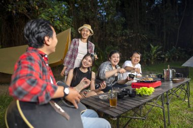 Endonezyalı güneydoğu Asyalılar ızgara tavada marine edilmiş et bulgogi pişiriyorlar. Bir tanesinin elinde akustik gitar var. Yemekten zevk alma yaşam tarzının doğal bir manzarası