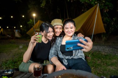 Endonezyalı Güneydoğu Asyalı kadınlar cep telefonlarını açık havada birlikte kullanarak selfie çekiyorlar ve içeceklerin tadını çıkarıyorlar. Doğal ortamdaki yemekten zevk alma sahnesi.