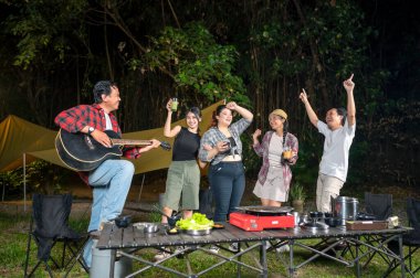 Endonezya 'nın güneydoğusundaki Asyalılar ferahlatıcı içeceklerin tadını çıkarıyorlar. Bir tanesinin elinde akustik gitar var. Yemekten zevk alma yaşam tarzının doğal bir manzarası