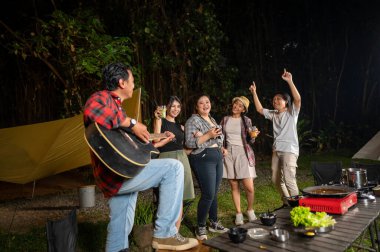 Endonezya 'nın güneydoğusundaki Asyalılar ferahlatıcı içeceklerin tadını çıkarıyorlar. Bir tanesinin elinde akustik gitar var. Yemekten zevk alma yaşam tarzının doğal bir manzarası