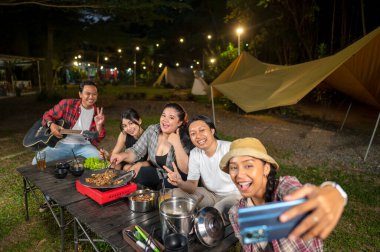 Endonezyalı güneydoğu Asyalılar dilimlenmiş sığır eti bulgogi pişirirken selfie çekiyorlar. Bir tanesinin elinde akustik gitar var. Yemekten zevk alma yaşam tarzının doğal bir manzarası