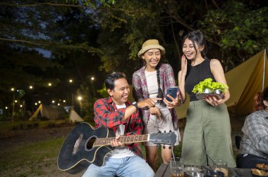 Endonezyalı güneydoğu Asyalılar birlikte güzel vakit geçiriyorlar. Adam gitarını tutuyor ve diğer kadınlar cep telefonunda bir şey gösteriyor. Doğal bir ortamda kamp yapmaktan hoşlanan bir yaşam tarzı.