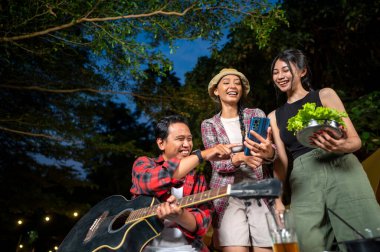 Endonezyalı güneydoğu Asyalılar birlikte güzel vakit geçiriyorlar. Adam gitarını tutuyor ve diğer kadınlar cep telefonunda bir şey gösteriyor. Doğal bir ortamda kamp yapmaktan hoşlanan bir yaşam tarzı.