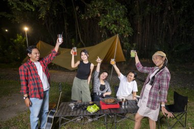 Endonezyalı güneydoğu Asyalılar birlikte dışarıda dinleniyor ve ızgara tavada dilimlenmiş et pişirirken taze içeceklerin tadını çıkarıyorlar. Doğal ortamdaki yemekten zevk alma sahnesi.