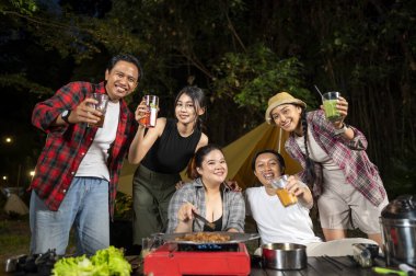 Endonezyalı güneydoğu Asyalılar birlikte dışarıda dinleniyor ve ızgara tavada dilimlenmiş et pişirirken taze içeceklerin tadını çıkarıyorlar. Doğal ortamdaki yemekten zevk alma sahnesi.