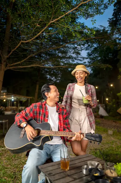 Endonezyalı güneydoğu Asyalı bir adam arkadaşlarıyla dışarıda akustik gitar çalıyor. Rahat ve keyifli bir yaşam tarzı gösteriyorum. Kamp yapmanın doğal ortamında keyif alma sahnesi.