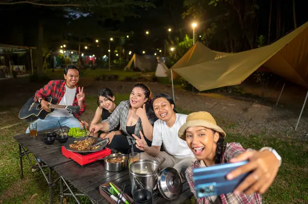 Endonezyalı güneydoğu Asyalılar dilimlenmiş sığır eti bulgogi pişirirken selfie çekiyorlar. Bir tanesinin elinde akustik gitar var. Yemekten zevk alma yaşam tarzının doğal bir manzarası