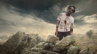 Yaralı ve kayalık arazide yürüyen korkunç erkek zombi. Sahne korkutucu ve ürkütücü. Dramatik bir gökyüzü. Ürkütücü Cadılar Bayramı kavramı