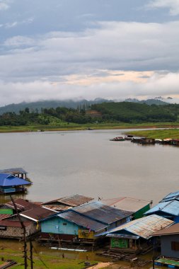 Durgun bir gölde, sis kaplı dağlarla çevrili yüzen evlerin sakin bir görüntüsü. Kayakçılar sakin suları keşfedip huzurlu ve huzurlu bir atmosfer yaratırlar..