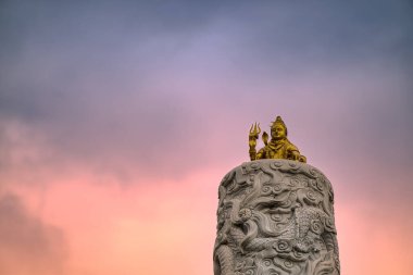 Lord Shiva 'nın görkemli bir heykeli süslü bir şekilde oyulmuş bir kaideye yerleştirilmiş, çarpıcı bir günbatımı gökyüzüne kurulmuş. Bu görüntü Hindu tanrısının güçlü ve huzurlu varlığını yakalar..