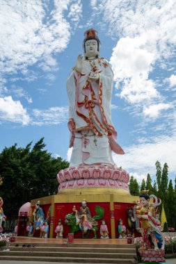 Chachoengsao, Tayland, Haziran 04, 2024, Wat Saman Rattanaram, yükselen beyaz Guan Yin heykeli, yemyeşil ve renkli tapınaklarla çevrili, canlı mavi gökyüzüne karşı dimdik ayakta duruyor. Merhamet ve merhametin simgesi olan bu sembol, ziyaret edilmesi gereken bir şeydir.