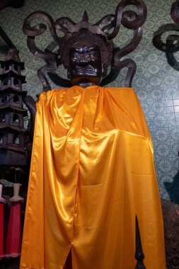 Chachoengsao, Thailand, June 04, 2024, Wat Chin Pracha Samoson, A striking image of a Buddhist deity statue with an intimidating expression, adorned with an elaborate headdress featuring intricate curls and spikes. The dark, wooden figure is draped i clipart