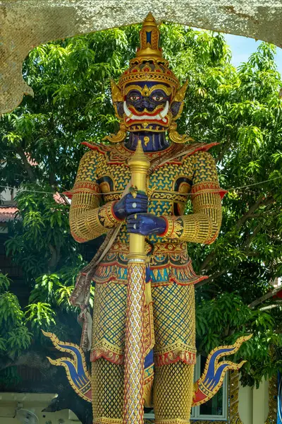 Chachoengsao, Tayland, Haziran 04, 2024, Wat Chuk Krachoe, Tapınaktaki Dev Muhafız Heykeli. Görkemli bir koruyucu heykel, berrak mavi gökyüzüne karşı karmaşık detaylar ve canlı renkler sunan geleneksel bir Tayland tapınağının önünde dimdik duruyor. Ka...