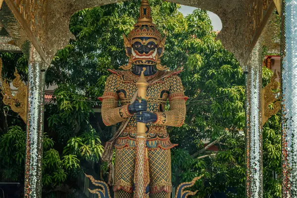 Chachoengsao, Tayland, Haziran 04, 2024, Wat Chuk Krachoe, Tapınaktaki Dev Muhafız Heykeli. Görkemli bir koruyucu heykel, berrak mavi gökyüzüne karşı karmaşık detaylar ve canlı renkler sunan geleneksel bir Tayland tapınağının önünde dimdik duruyor. Ka...