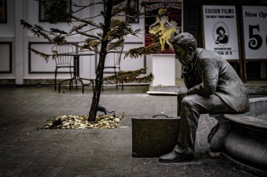 Klasik film posterleri ve küçük bir ağaçla süslenmiş, sakin bir avludaki taş bir bankta duraklayan düşünceli bir figürün heykeli..