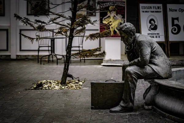 Klasik film posterleri ve küçük bir ağaçla süslenmiş, sakin bir avludaki taş bir bankta duraklayan düşünceli bir figürün heykeli..