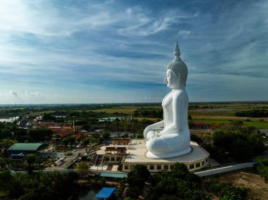 Büyük beyaz Buda heykeli, Tayland 'ın Ang Thong kentindeki yeşillik ve tarım arazileriyle çevrili bir tepenin üzerinde huzur içinde duruyor. Ayar Nisan ayında açık bir gökyüzü altında huzurlu bir görünüm sunuyor.