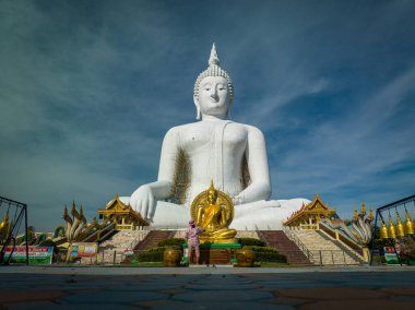 Ziyaretçiler, Ang Thong, Tayland 'daki Wat Muang' daki görkemli beyaz Buda heykeline hayran, güneşli bir nisan gününde altın ayrıntılar ve yemyeşil ile çevrili..