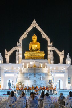 Puttha Sathan Lopburi 'deki altın Buda heykelinin önünde toplanan ibadet edenler gece gökyüzü altında bağlılık ve huzur dolu bir törene katılıyorlar..