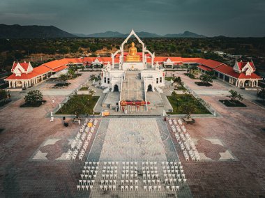Alacakaranlıkta Puttha Sathan Lopburi Sri Suvarnabhumi 'nin geniş bir manzarası var. Yeşillik ve çarpıcı mimariyle çevrili bir akşam toplantısı için dizilmiş sandalyeler var..