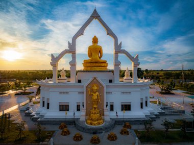 Puttha Sathan Lopburi, Tayland 'da baş döndürücü bir altın Buda heykeli duruyor. Batan güneşin yumuşak parıltısı etrafındaki sakin manzarayı aydınlatıyor..