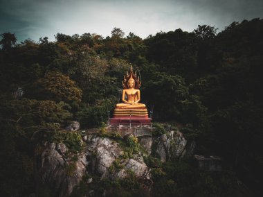 Tayland 'ın Nakhon Sawan kentindeki sık ağaçlarla çevrili kayalık bir çıkıntının tepesinde sakin bir Buda heykeli duruyor..