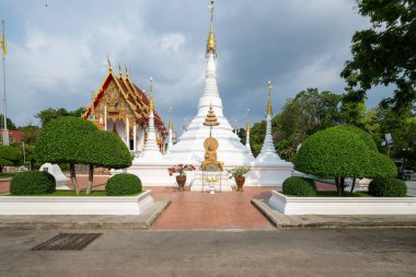 Entrika ile tasarlanmış stupa, Tayland 'ın Nonthaburi şehrinde parçalı bulutlu bir gökyüzü altında düzgün budanmış çalılar ve geleneksel Tayland yapılarıyla çevrili Wat Chomphuwek' te belirgin bir şekilde duruyor..