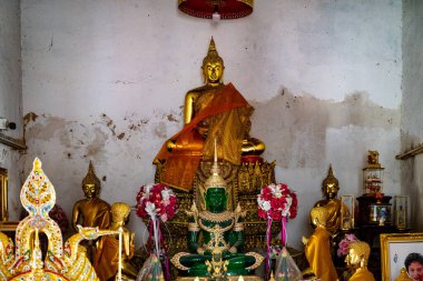 Wat Chimphli Sutthawat 'ın içinde, turuncu bir cübbeye bürünmüş merkezi bir figür de dahil olmak üzere altın Budist heykeller barışçıl bir atmosfer yaratıyor. İdollerin etrafını saran çiçekler..