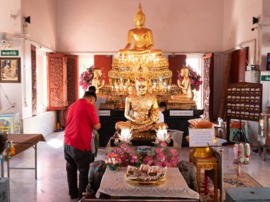 Huzurlu bir tapınağın içinde, büyük bir altın Buda heykeli ibadet edenlerin sundukları ve huzurlu bir atmosfer ve sıcak güneş ışığı altında dua ettikleri odak noktasıdır..