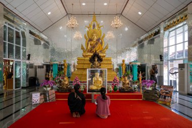 Tayland 'ın Phra Nakhon Si Ayutthaya kentindeki Wat Na Tang Nok' ta bulunan büyük bir Buda heykelinin önünde kırmızı halıya iki kişi diz çöker. Huzurlu atmosfer bağlılıklarını arttırır..