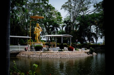 Singburi, Tayland 'daki Wat Phikun Tangası' nda sakin bir göletin yanında altın bir heykel duruyor. Bölgeyi çevreleyen yemyeşil ağaçlar Mart ayında huzurlu bir atmosfer yaratıyor..