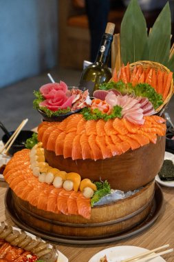 Muhteşem bir suşi düzeninde taze somon, karides ve ton balığı katmanlı ahşap tabakta servis edilir. Bu canlı deniz ürünleri sergisi öğle yemeği için canlı bir restoran atmosferinde sunuluyor..