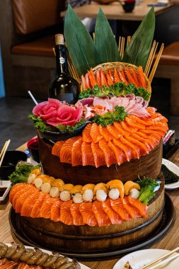 Çok güzel düzenlenmiş deniz ürünleri tabakları sayısız taze somon dilimleri ve yeşilliklerle süslenmiş ve bir restoran masasında yemek çubukları eşliğinde saşimi sergileniyor..