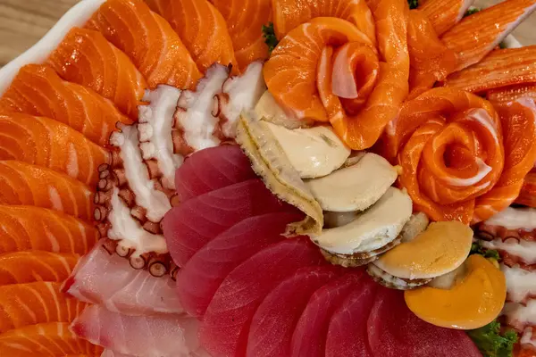 Canlı bir sashimi tabağında somon, ton balığı ve ahtapot gibi taze deniz ürünleri sergileniyor. Renk ve dokusunu vurgulamak için güzelce düzenlenmiş. Suşi severler için mükemmel..