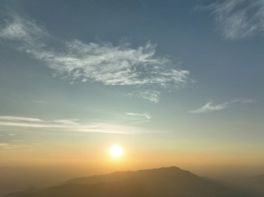 Güneş uzak dağların üzerinde batar, sıcak altın bir parıltı yayar gökyüzünde. Yumuşak bulutlar ışığı yansıtır. Huzurlu bir akşam atmosferi yaratır. Yansıma için mükemmel..