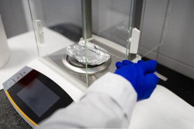 Bir bilim adamının beyaz katı bir numuneyi tartmasının detaylı görünümü