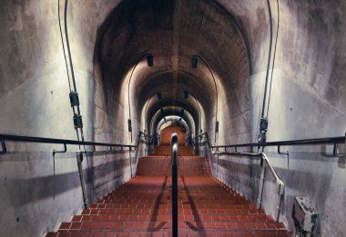 Kırmızı tuğlalı merdivenleri ve metal tırabzanları olan bir yeraltı tüneli..