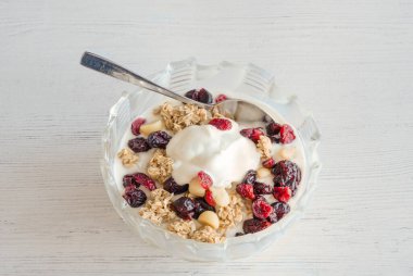 Bir kase dolusu çam fıstıklı yoğurt kurutulmuş yaban mersini ve kuru üzümle dolu ideal, küçük gümüş kaşıkla servis edilen modern kahvaltı..