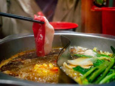 İnsan eli yemek çubuğu kullanarak restoranın masasındaki Sichuan mala soslu shabu 'nun üzerinde et tutar..